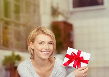 Eine blonde Frau hält lächelnd einen Geschenkgutschein in den Händen