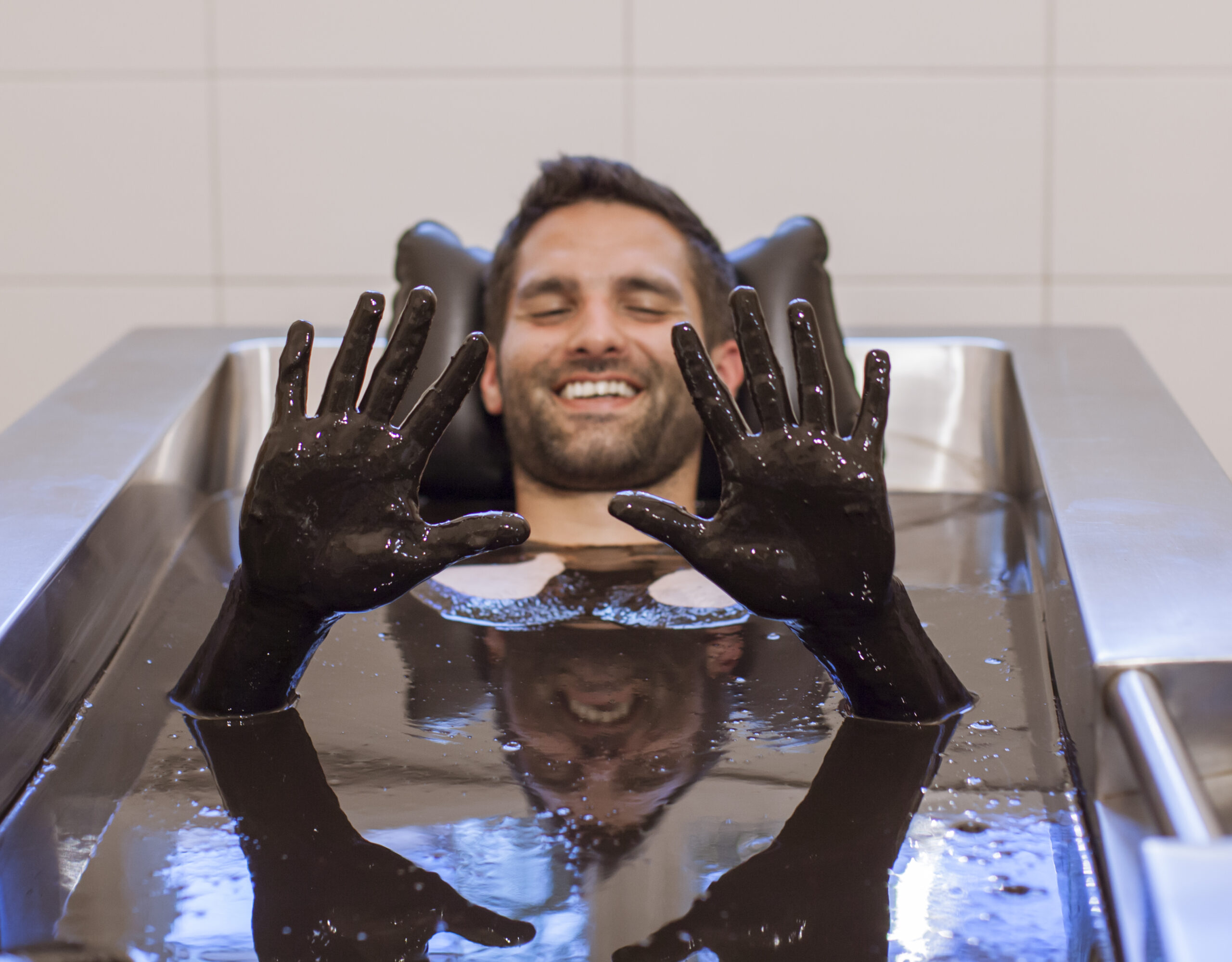 Ein Mann liegt lächelnd in einer Naturmoor-Badewanne