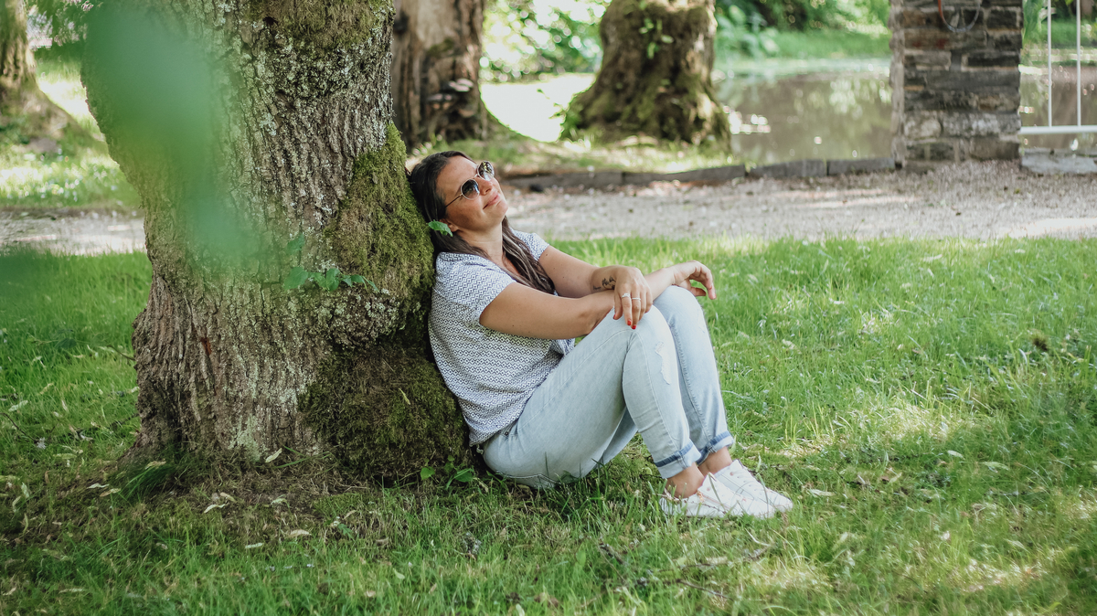 Eine Frau sitzt entspannt mit dem Rücken an einem Baum