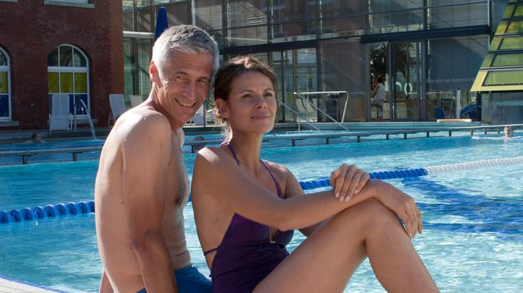 Ein Paar mittleren Alters sitzt entspannt draußen am Schwimmbecken