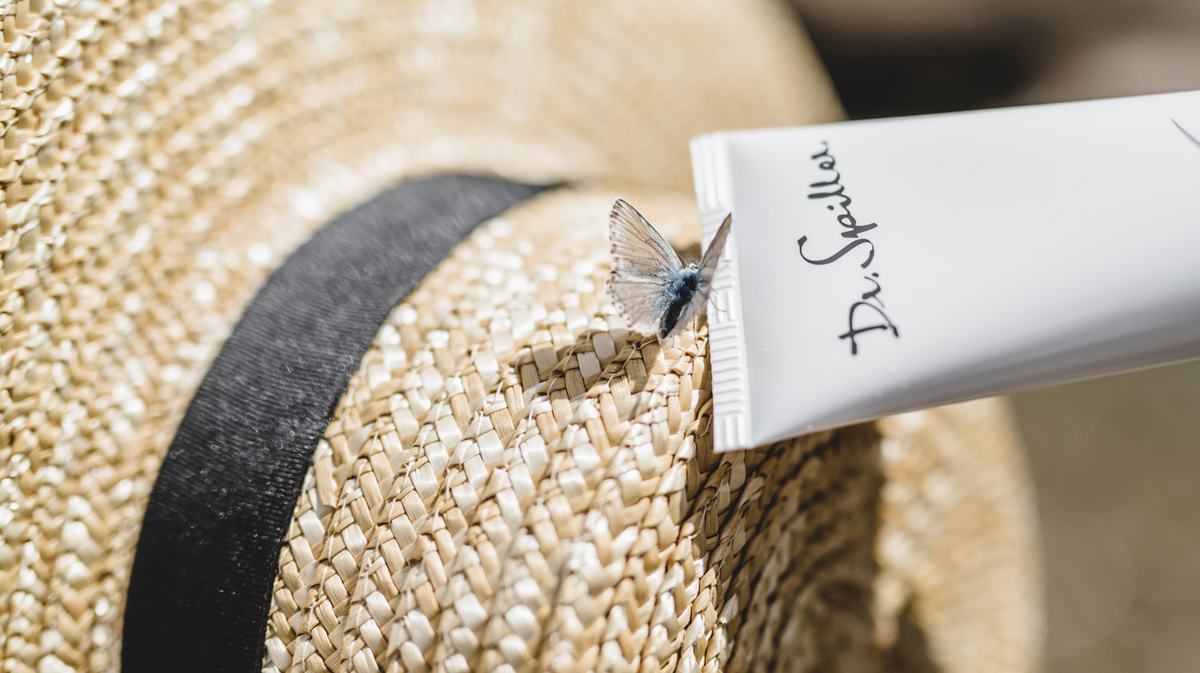 Auf einem Strohhut sitzt ein kleiner Schmetterling und krabbelt auf eine Dr. Spiller Cremetube