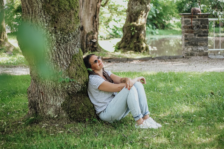 Eine Frau lehnt mit dem Rücken sitzend an einem Baum