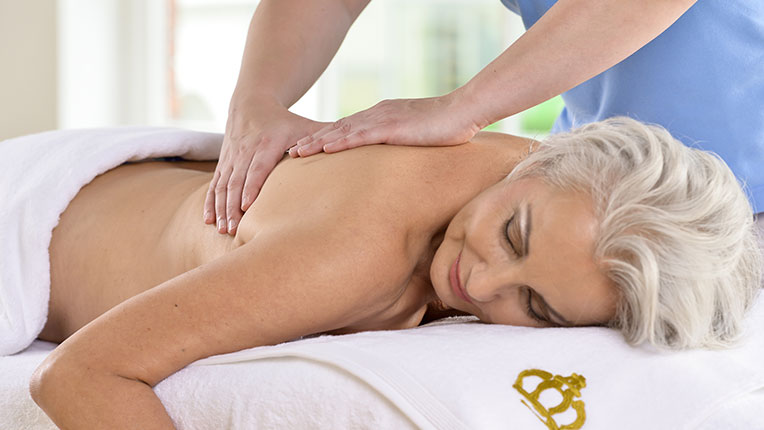 Eine ältere Dame mit grauem kurzen Haar wird am Rücken auf einer Liege massiert