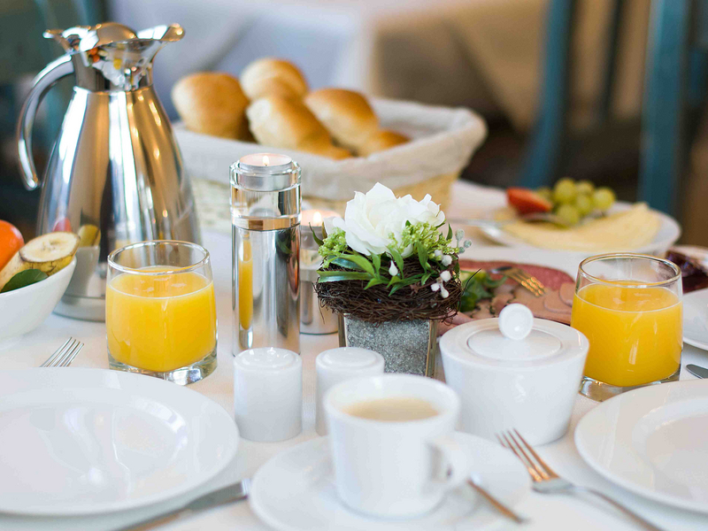 Gedeckter Frühstückstisch mit Kaffee, Orangensaft, Brötchen, Käse, Wurst