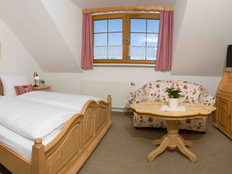 Zimmerbeispiel mit Holz-Doppelbett, kleinem Sofa, Tisch und TV