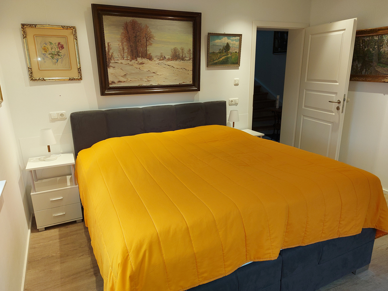 Graues Stoff-Doppelbett mit einer orangenen Tagesdecke in einem weißen Schlafzimmer