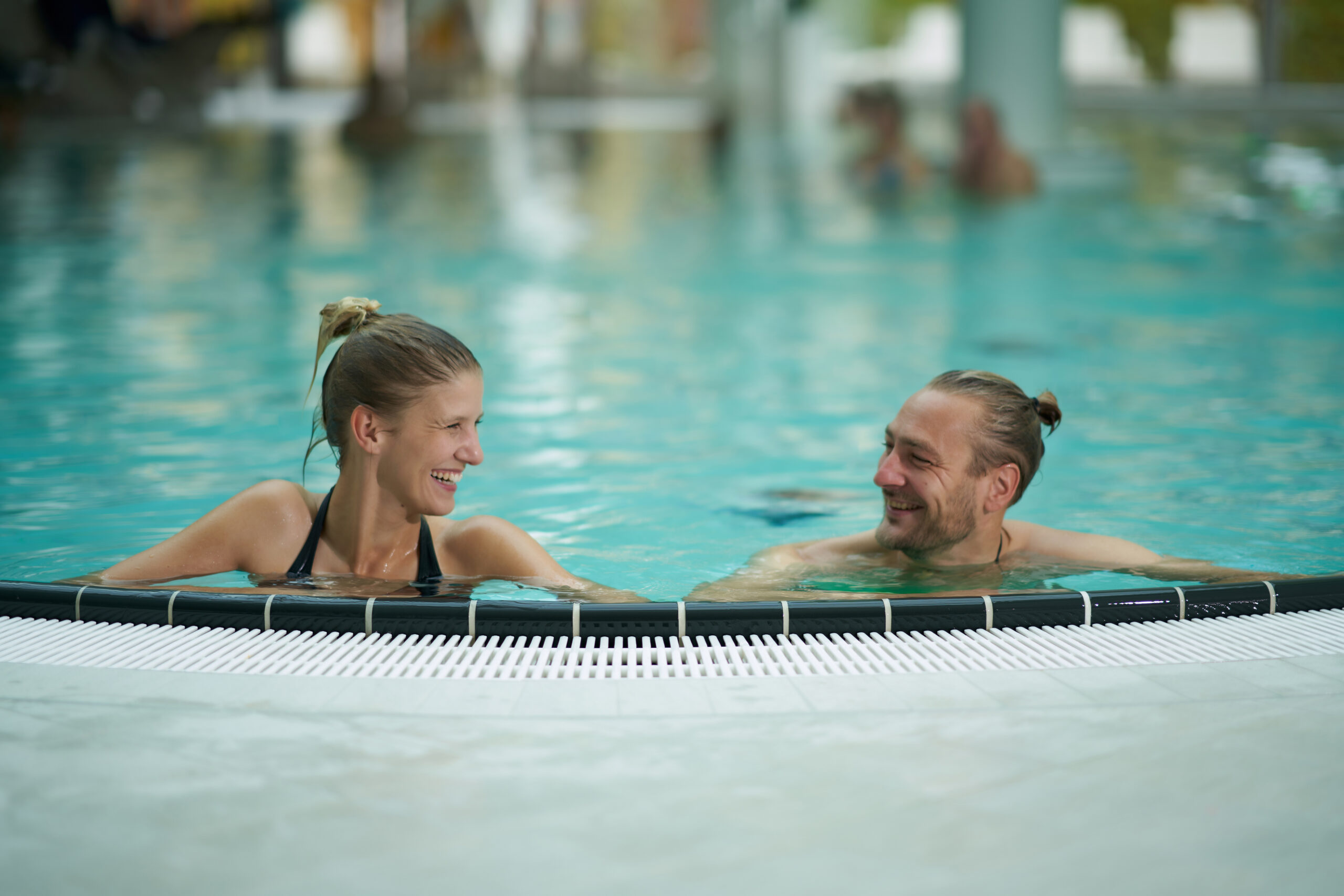 Ein Paar am Rand vom Schwimmbecken, sich glücklich anlächelnd