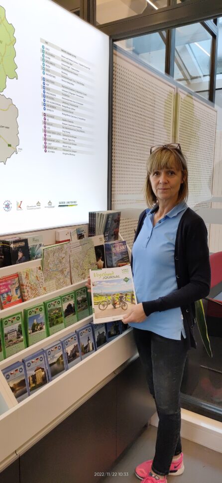 Eine Frau steht vor einem Regal mit Informationsbroschüren und hält eine in der Hand