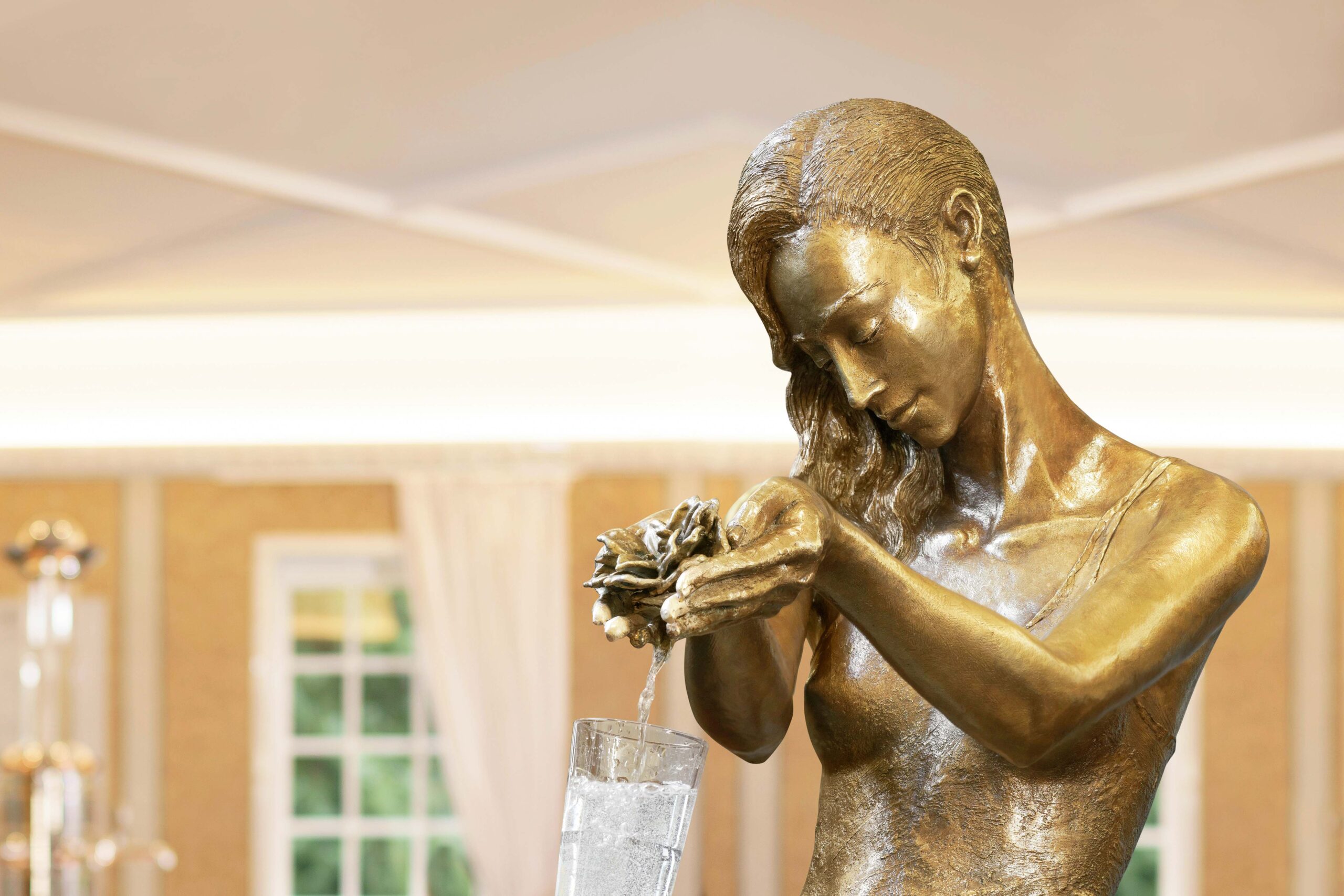 Frauenstatue aus deren Hände Wasser in ein Glas läuft