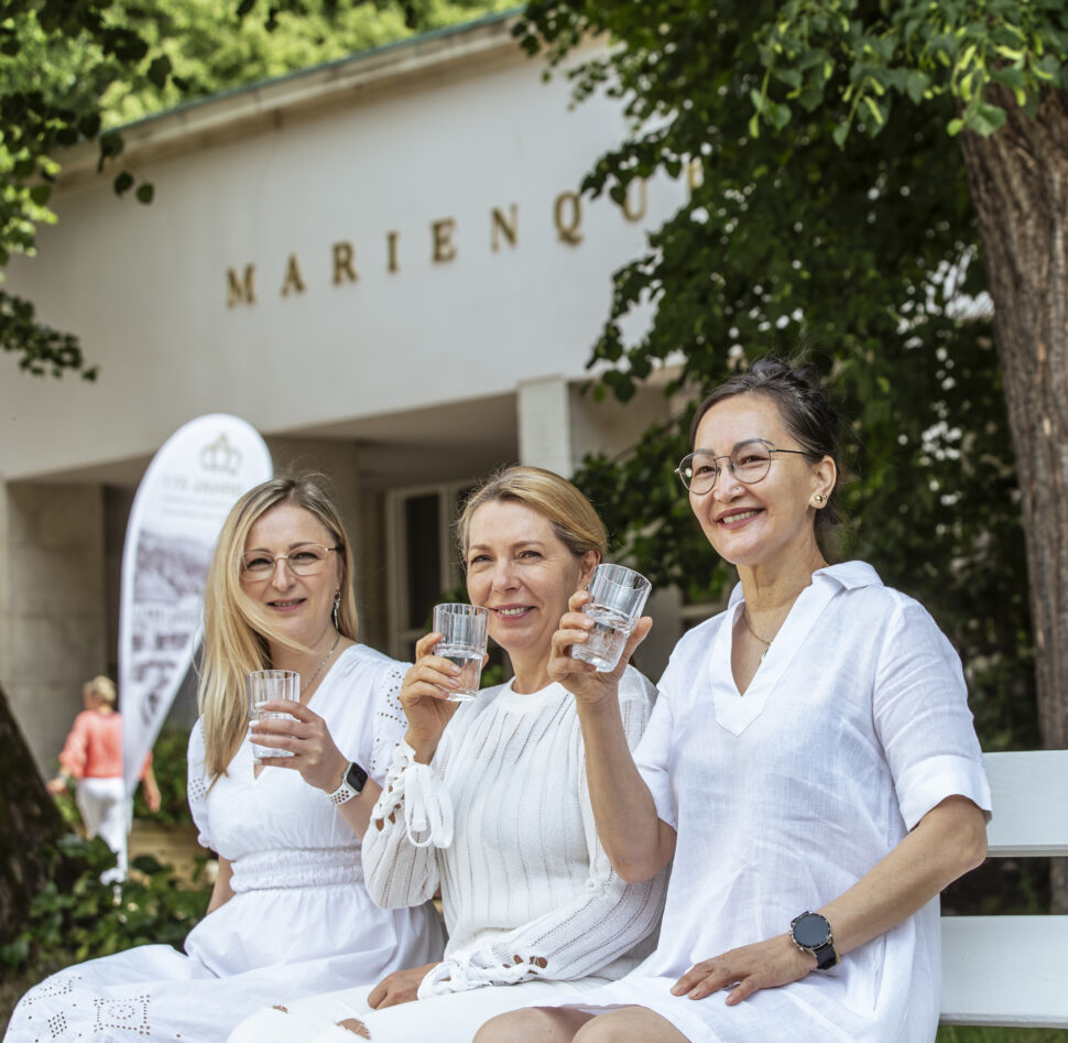 Drei Frauen sitzen auf einer Bank vor der Marienquelle und trinken Mineralheilwasser